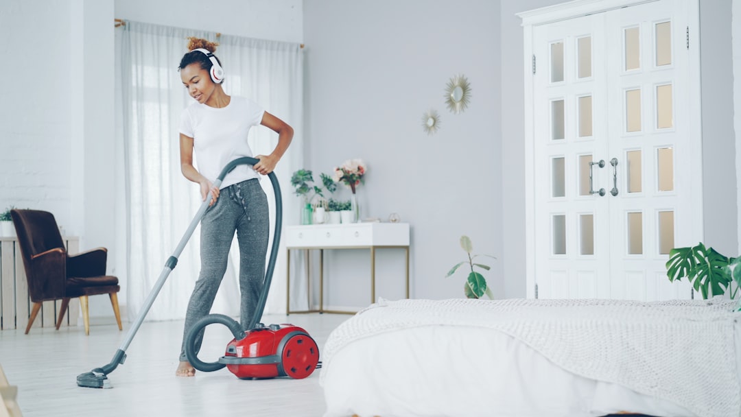 Creative African American teenager is hoovering floor in nice apartment, listening to music with headphones, dancing and singing. Electrical appliances, clean-up and fun concept.